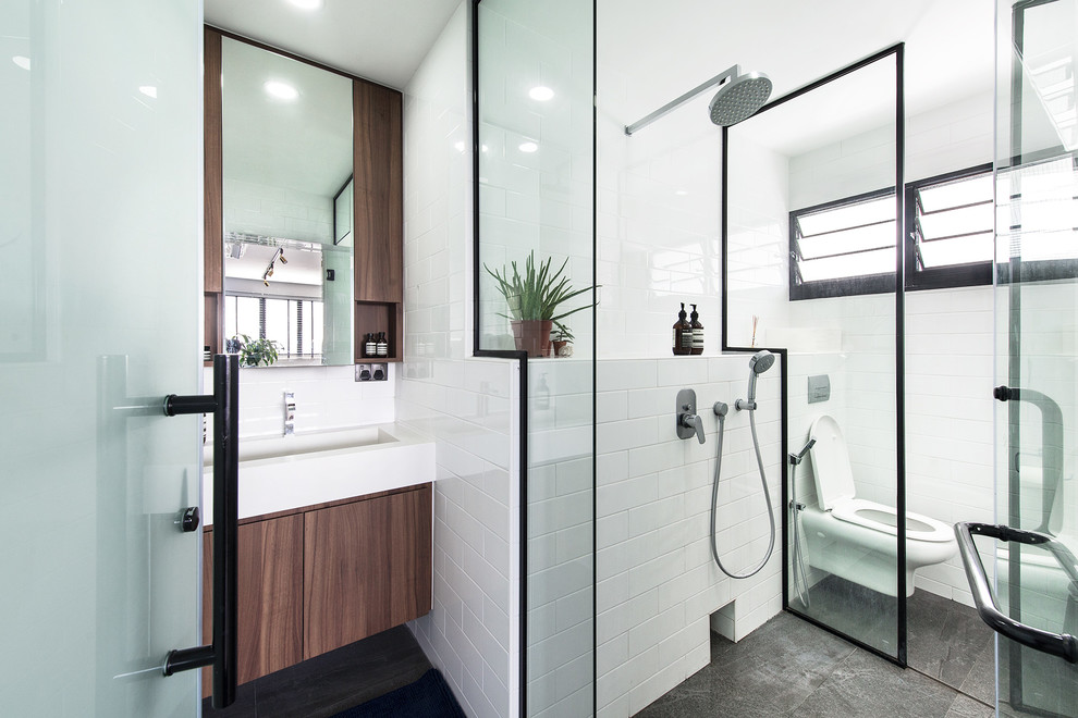 Exempel på ett modernt badrum med dusch, med släta luckor, skåp i mörkt trä, våtrum, en vägghängd toalettstol, vit kakel, tunnelbanekakel, vita väggar, ett konsol handfat, grått golv och dusch med gångjärnsdörr