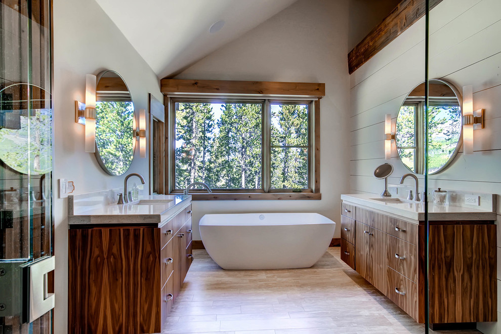 На фото: ванная комната в стиле рустика с врезной раковиной, плоскими фасадами, темными деревянными фасадами, отдельно стоящей ванной, серыми стенами и зеркалом с подсветкой