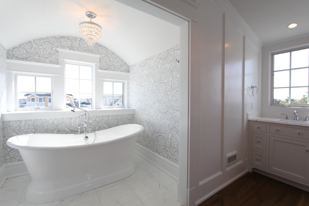 Cette image montre une salle de bain principale marine avec un placard à porte affleurante, des portes de placard blanches, une baignoire indépendante, une douche ouverte, WC séparés, un mur gris, un sol en marbre, un lavabo encastré et un plan de toilette en marbre.