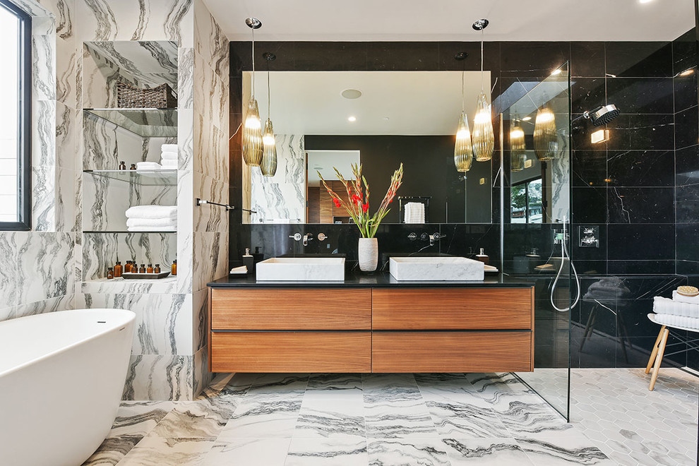 Inredning av ett modernt en-suite badrum, med släta luckor, skåp i mellenmörkt trä, ett fristående badkar, en öppen dusch, svart kakel, svart och vit kakel, flerfärgade väggar, ett fristående handfat, flerfärgat golv och med dusch som är öppen