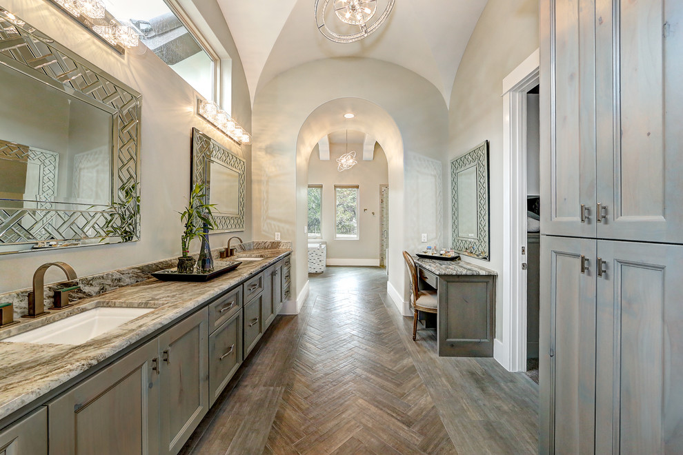 Inspiration for a huge timeless master medium tone wood floor and brown floor drop-in bathtub remodel in Austin with recessed-panel cabinets, gray cabinets, a two-piece toilet, beige walls, an undermount sink and granite countertops