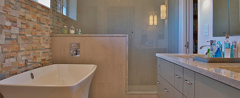 Foto på ett 50 tals badrum, med ett undermonterad handfat, släta luckor, grå skåp, granitbänkskiva, ett fristående badkar, en öppen dusch, en toalettstol med separat cisternkåpa, grå kakel och porslinskakel