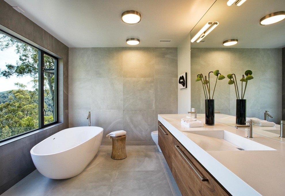Aménagement d'une salle de bain principale contemporaine en bois brun avec un placard à porte plane, une baignoire indépendante, un lavabo intégré et une fenêtre.