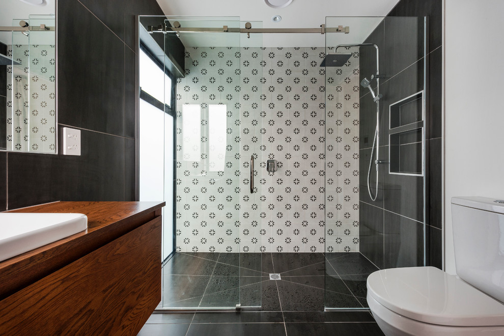 Modernes Duschbad mit flächenbündigen Schrankfronten, dunklen Holzschränken, Duschnische, Wandtoilette mit Spülkasten, schwarz-weißen Fliesen, weißer Wandfarbe, Einbauwaschbecken, schwarzem Boden und Schiebetür-Duschabtrennung in Auckland
