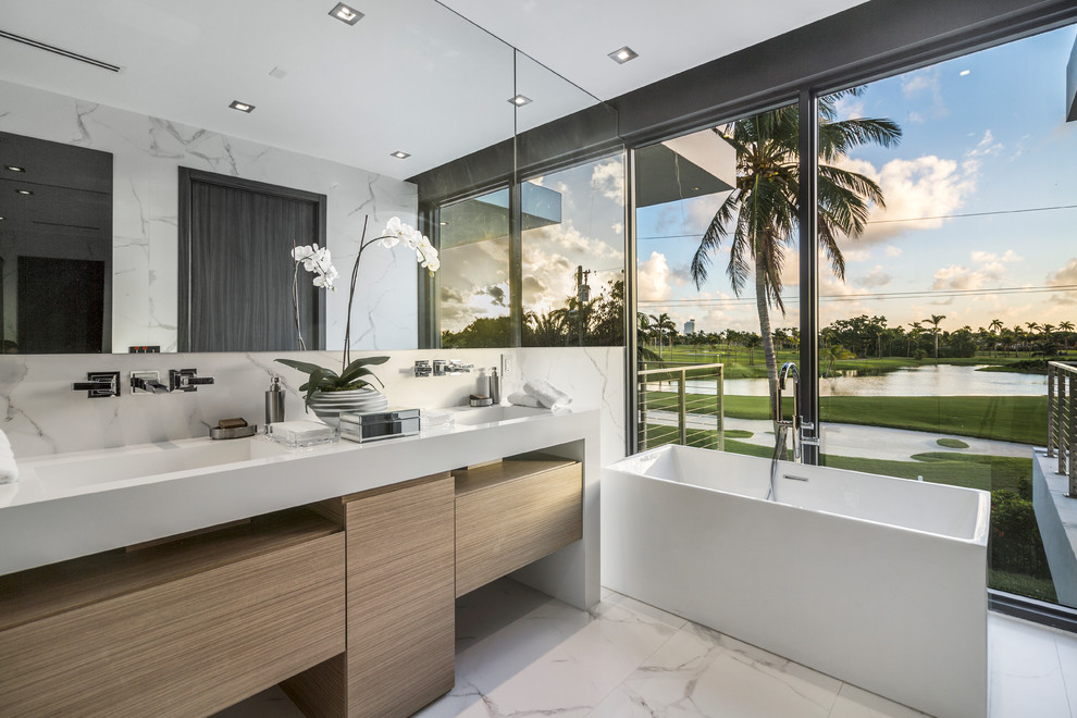 Modernes Badezimmer mit flächenbündigen Schrankfronten, beigen Schränken, freistehender Badewanne, integriertem Waschbecken, weißem Boden und weißer Waschtischplatte in Miami