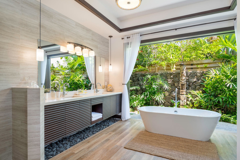 Idee per una stanza da bagno tropicale con ante lisce, ante in legno bruno, vasca freestanding, piastrelle grigie, pareti bianche, lavabo sottopiano, pavimento beige e top bianco
