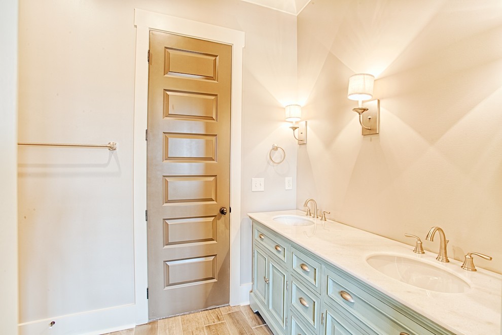 Modelo de cuarto de baño principal tradicional de tamaño medio con armarios con rebordes decorativos, paredes beige, suelo de madera clara, lavabo bajoencimera, encimera de cuarcita y puertas de armario turquesas