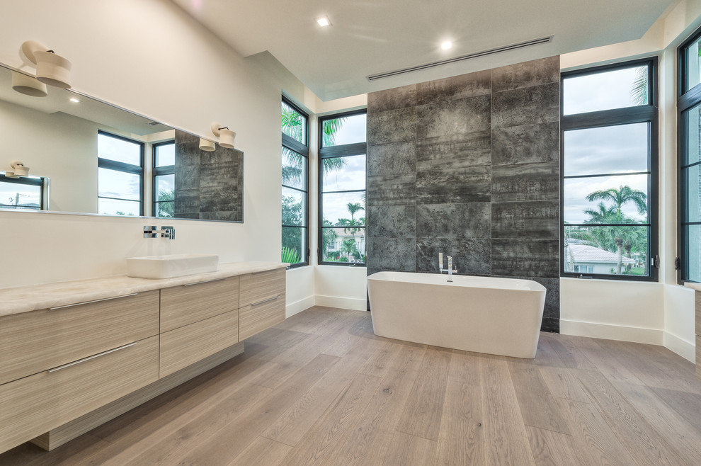 This is an example of a large modern ensuite bathroom in Miami with flat-panel cabinets, beige cabinets, a freestanding bath, an alcove shower, a one-piece toilet, white tiles, ceramic tiles, white walls, light hardwood flooring, a vessel sink, granite worktops and brown floors.