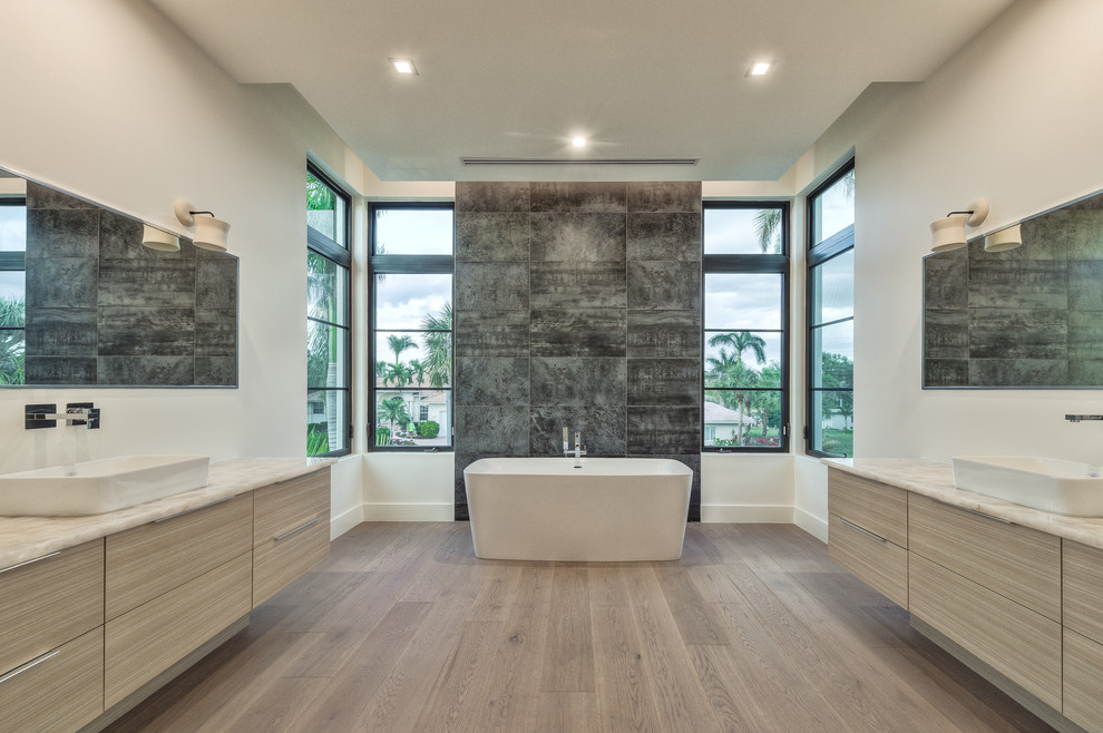 Inspiration för stora moderna en-suite badrum, med ett fristående badkar, en dusch i en alkov, en toalettstol med hel cisternkåpa, vit kakel, keramikplattor, vita väggar, ljust trägolv, ett fristående handfat, brunt golv, släta luckor, beige skåp och granitbänkskiva