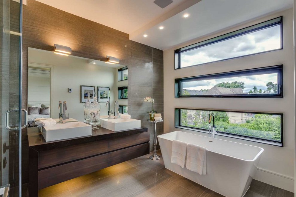 Пример оригинального дизайна: главная ванная комната среднего размера в стиле модернизм с плоскими фасадами, темными деревянными фасадами, отдельно стоящей ванной, угловым душем, раздельным унитазом, белой плиткой, белыми стенами, стеклянной столешницей, полом из керамогранита и настольной раковиной