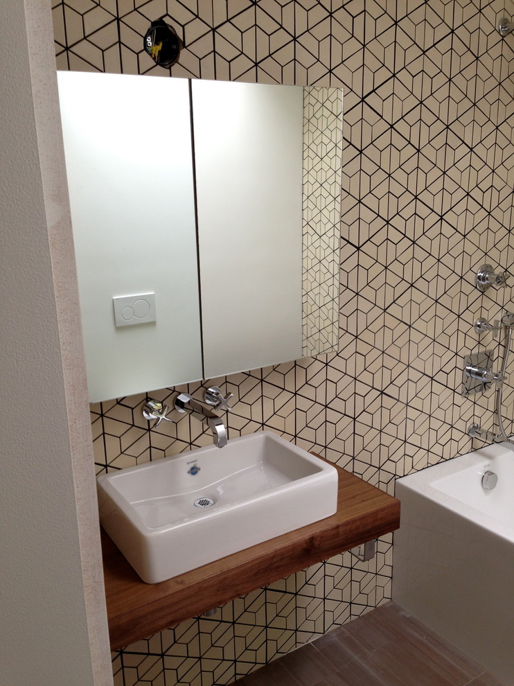 Foto di una stanza da bagno minimalista con lavabo a consolle, ante lisce, ante in legno bruno, top in legno, vasca ad angolo, vasca/doccia e WC sospeso