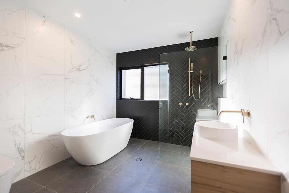 На фото: ванная комната в современном стиле с светлыми деревянными фасадами, отдельно стоящей ванной, душем без бортиков, черной плиткой, белой плиткой, настольной раковиной, серым полом, душем с распашными дверями и белой столешницей