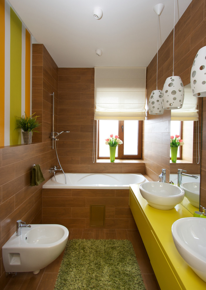 Idéer för att renovera ett eklektiskt gul gult badrum, med ett fristående handfat, släta luckor, gula skåp, ett badkar i en alkov, en dusch/badkar-kombination, en bidé, bruna väggar och mellanmörkt trägolv