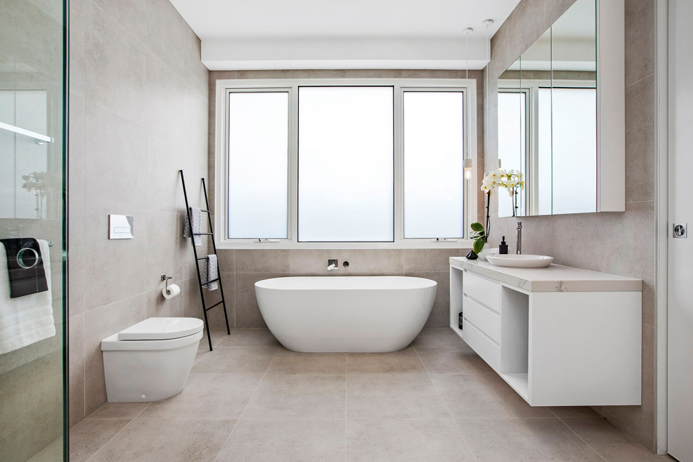 Inspiration för moderna beige badrum, med släta luckor, vita skåp, ett fristående badkar, beige kakel, ett fristående handfat och grått golv