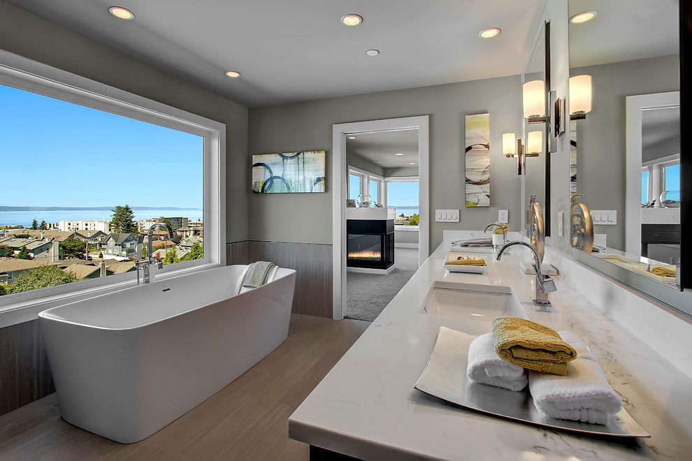 На фото: главная ванная комната в современном стиле с отдельно стоящей ванной, серыми стенами, светлым паркетным полом, врезной раковиной и мраморной столешницей с
