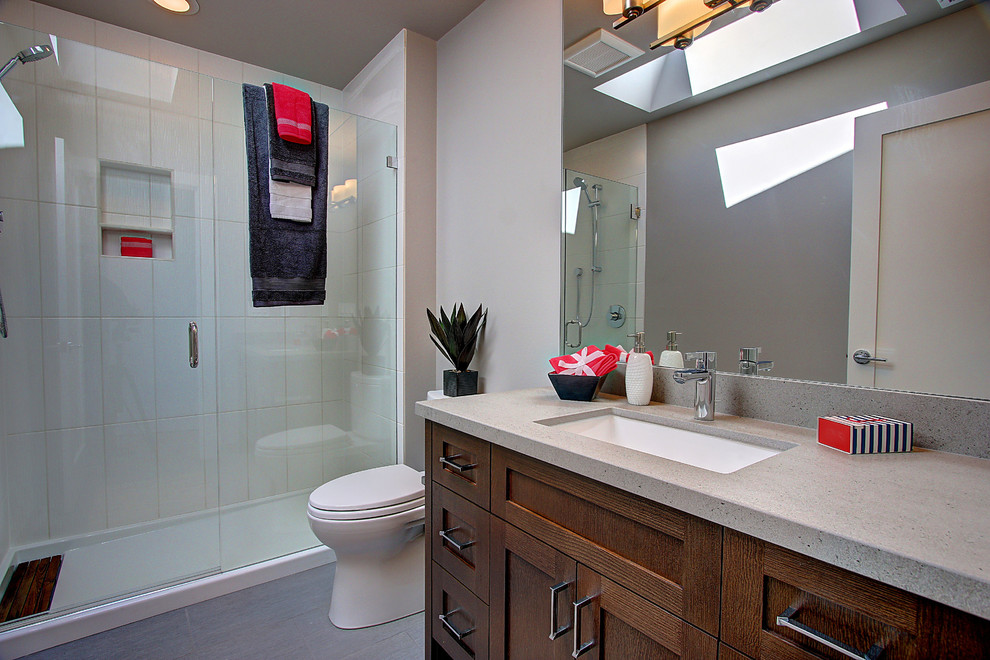 Cette image montre une salle de bain traditionnelle en bois brun avec un placard à porte shaker, un carrelage beige, un mur gris, un lavabo encastré, une cabine de douche à porte battante et un plan de toilette gris.