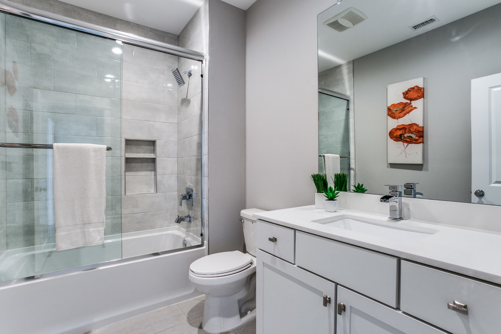 Medium sized traditional shower room bathroom in Dallas with shaker cabinets, white cabinets, an alcove bath, a shower/bath combination, a two-piece toilet, grey tiles, stone tiles, grey walls, porcelain flooring, a submerged sink, beige floors, a sliding door, marble worktops, white worktops, a single sink and a built in vanity unit.