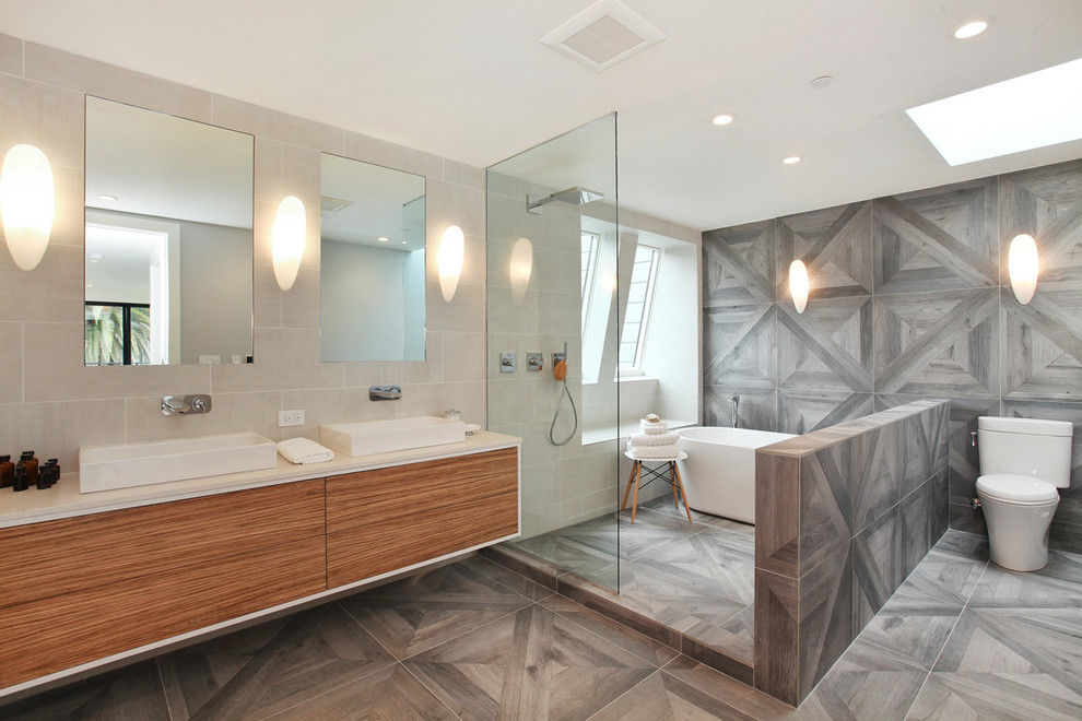 На фото: ванная комната в современном стиле с настольной раковиной, плоскими фасадами, фасадами цвета дерева среднего тона, отдельно стоящей ванной, открытым душем, серой плиткой и открытым душем с