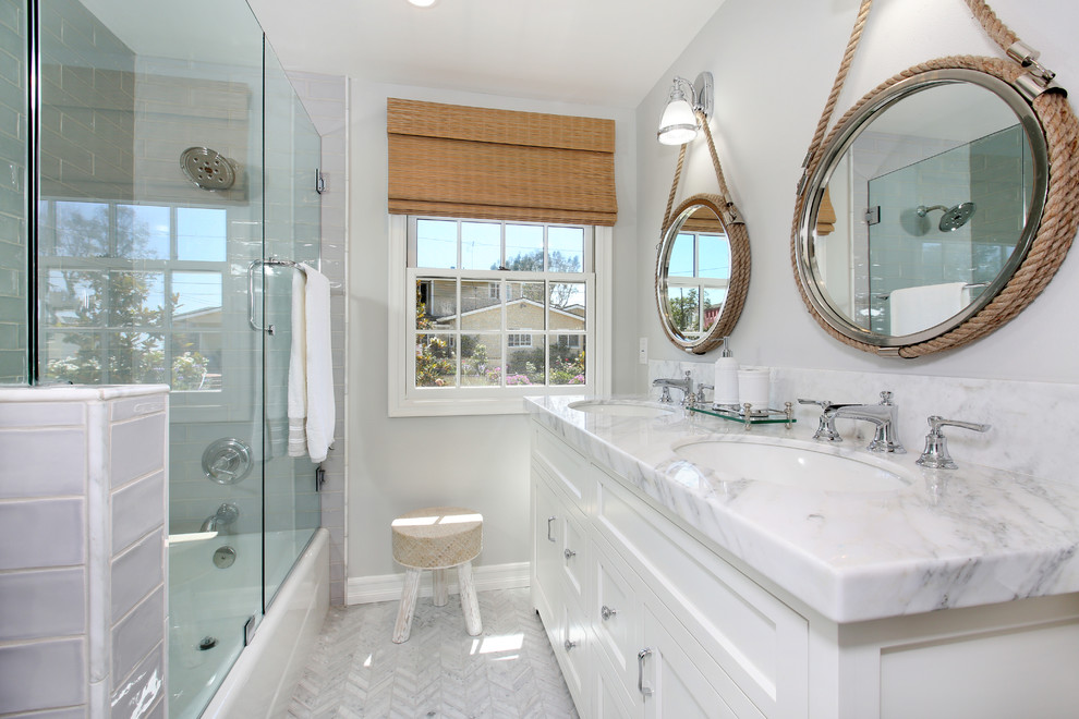 Пример оригинального дизайна: ванная комната в морском стиле с фасадами с выступающей филенкой, белыми фасадами, душем над ванной, серой плиткой, керамической плиткой, серыми стенами, врезной раковиной и мраморной столешницей