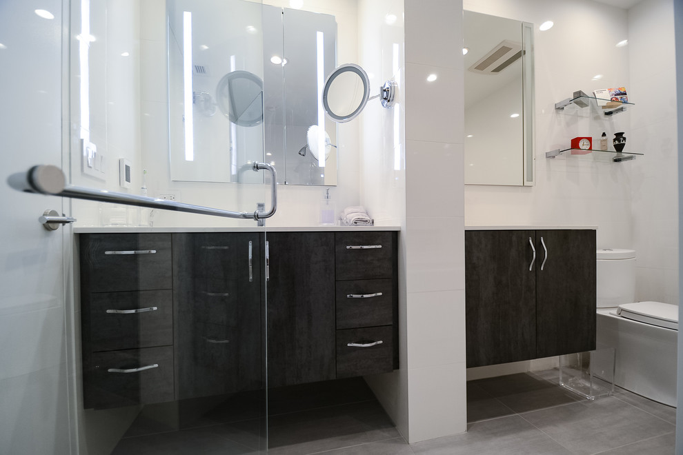 Design ideas for a large modern ensuite bathroom in New York with flat-panel cabinets, dark wood cabinets, an alcove bath, an alcove shower, a one-piece toilet, white tiles, glass tiles, white walls, porcelain flooring, a submerged sink, quartz worktops, grey floors, a hinged door and yellow worktops.