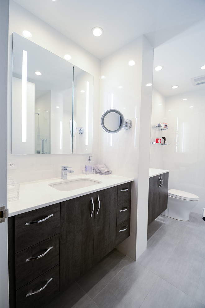 Photo of a large modern ensuite bathroom in New York with flat-panel cabinets, dark wood cabinets, an alcove bath, an alcove shower, a one-piece toilet, white tiles, glass tiles, white walls, porcelain flooring, a submerged sink, quartz worktops, grey floors, a hinged door and yellow worktops.