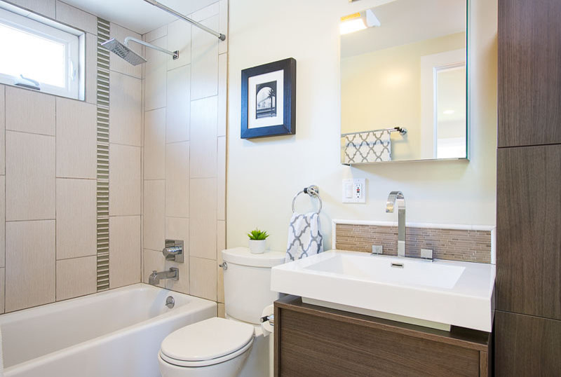 Modern inredning av ett litet en-suite badrum, med ett väggmonterat handfat, släta luckor, grå skåp, bänkskiva i akrylsten, ett badkar i en alkov, en toalettstol med separat cisternkåpa, grå kakel, stenkakel, gröna väggar och klinkergolv i keramik