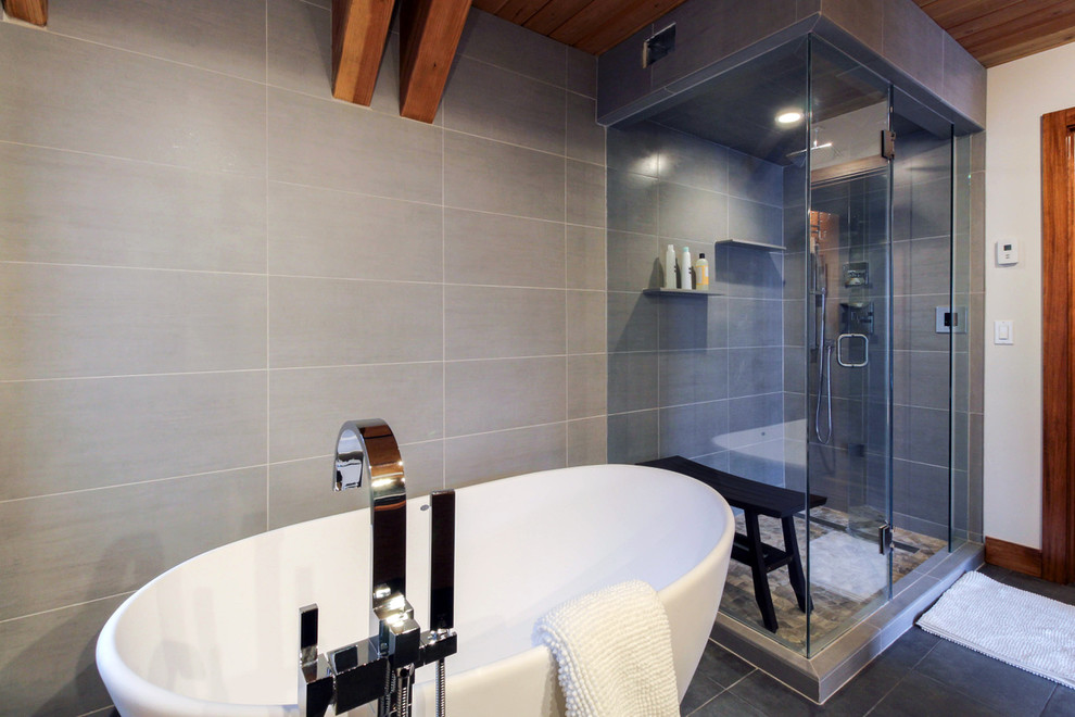 Cette photo montre une salle de bain principale chic de taille moyenne avec une baignoire indépendante, une douche d'angle, un carrelage gris, des carreaux de porcelaine, un mur gris, un sol en carrelage de porcelaine, un sol gris et une cabine de douche à porte battante.