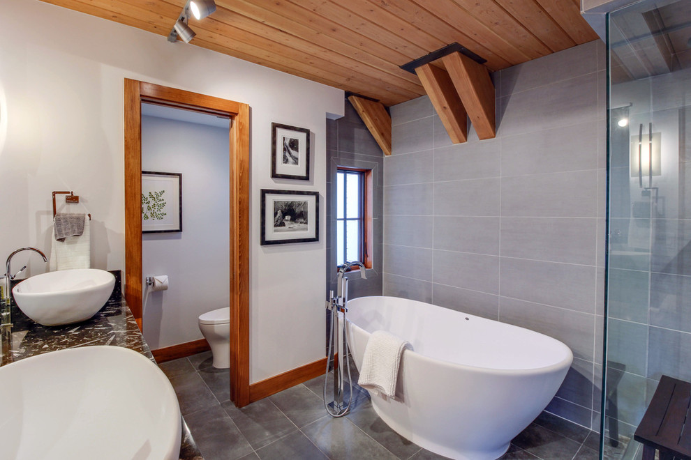 На фото: главная ванная комната среднего размера в стиле неоклассика (современная классика) с отдельно стоящей ванной, угловым душем, унитазом-моноблоком, серой плиткой, керамогранитной плиткой, серыми стенами, полом из керамогранита, настольной раковиной, серым полом, душем с распашными дверями и черной столешницей с