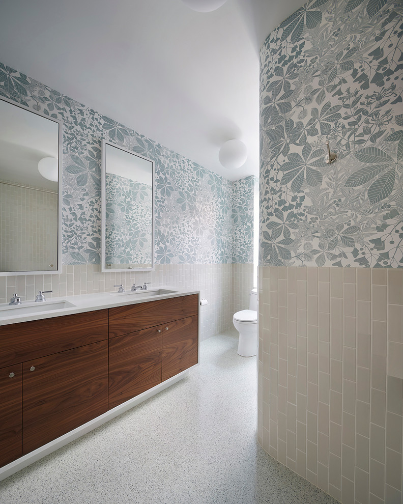 Inspiration pour une salle de bain design en bois foncé avec un placard à porte plane, un mur multicolore, un lavabo encastré, WC à poser, un carrelage beige, des carreaux de céramique et un plan de toilette en surface solide.