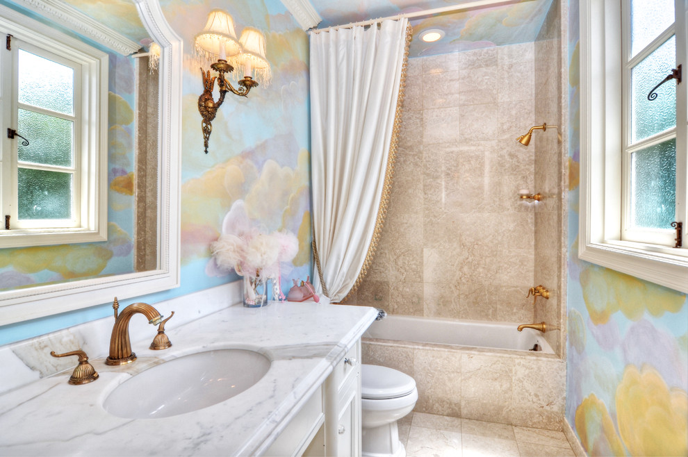 Modelo de cuarto de baño infantil mediterráneo de tamaño medio con puertas de armario blancas, encimera de mármol, bañera encastrada, baldosas y/o azulejos beige, paredes multicolor y suelo de travertino