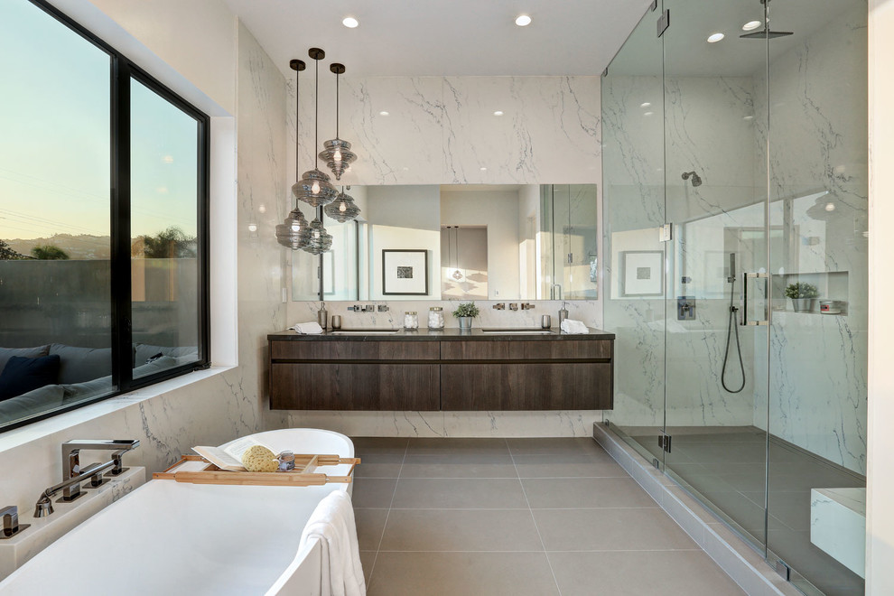 Cette image montre une salle de bain principale design en bois foncé avec un placard à porte plane, une baignoire indépendante, un espace douche bain, un mur blanc, un lavabo encastré, un sol gris et une cabine de douche à porte battante.