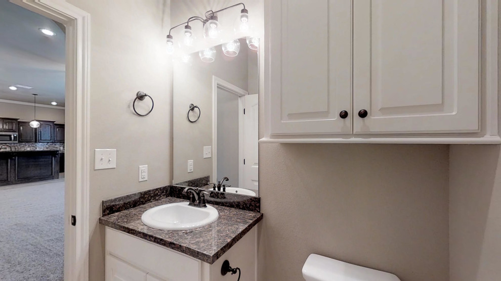 Cette image montre une petite salle de bain traditionnelle avec un placard avec porte à panneau surélevé, des portes de placard blanches, un mur beige, un sol en carrelage de céramique, un lavabo posé, un plan de toilette en granite, un sol beige et un plan de toilette noir.