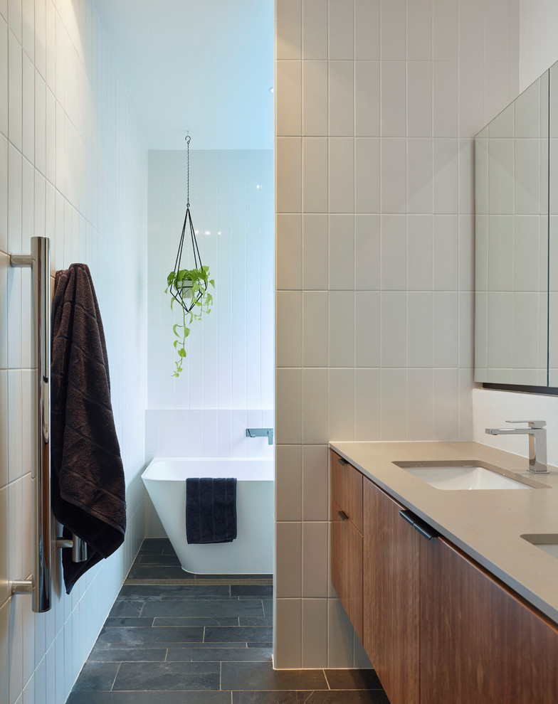 Photo of a contemporary bathroom in Brisbane with flat-panel cabinets, medium wood cabinets, a freestanding bath, white tiles, white walls, a submerged sink, grey floors and beige worktops.
