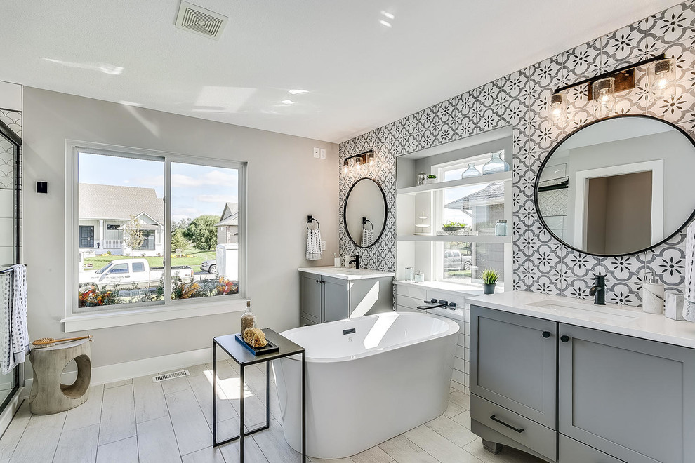 Inspiration for a large modern ensuite bathroom in Wichita with flat-panel cabinets, grey cabinets, a freestanding bath, an alcove shower, a one-piece toilet, multi-coloured tiles, ceramic tiles, grey walls, ceramic flooring, a built-in sink, quartz worktops, grey floors, a sliding door and white worktops.