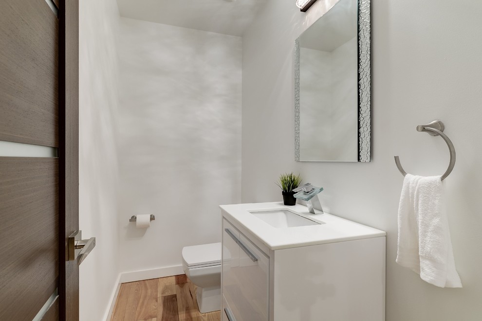 Foto di una stanza da bagno con doccia contemporanea di medie dimensioni con ante lisce, ante bianche, WC a due pezzi, pareti bianche, parquet chiaro, lavabo sottopiano e top in superficie solida