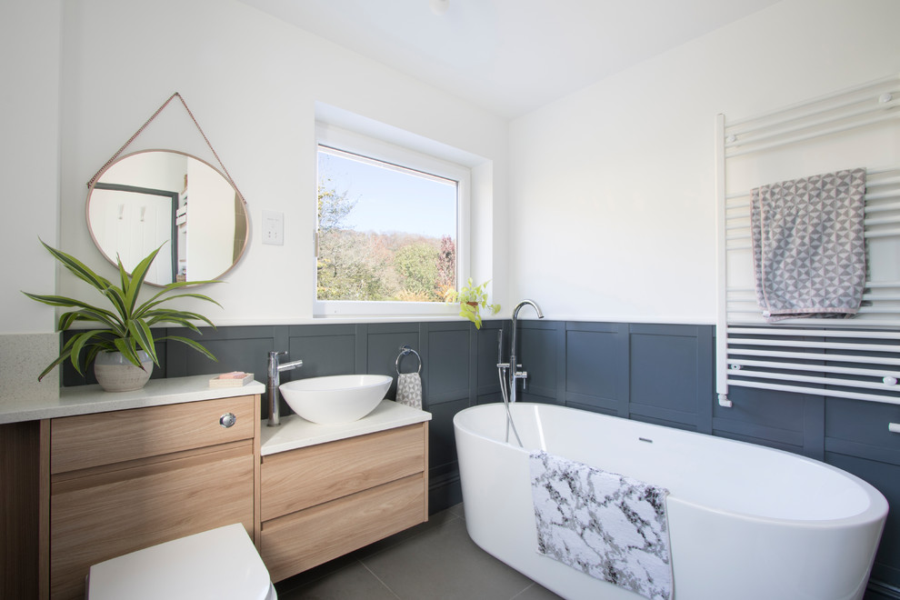 Пример оригинального дизайна: ванная комната в современном стиле с плоскими фасадами, светлыми деревянными фасадами, отдельно стоящей ванной, белыми стенами, настольной раковиной, серым полом и белой столешницей
