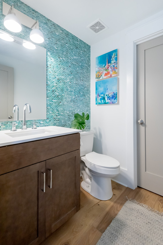Inspiration for a medium sized beach style shower room bathroom in Charleston with shaker cabinets, dark wood cabinets, a two-piece toilet, green tiles, glass tiles, white walls, light hardwood flooring, an integrated sink, engineered stone worktops and white worktops.