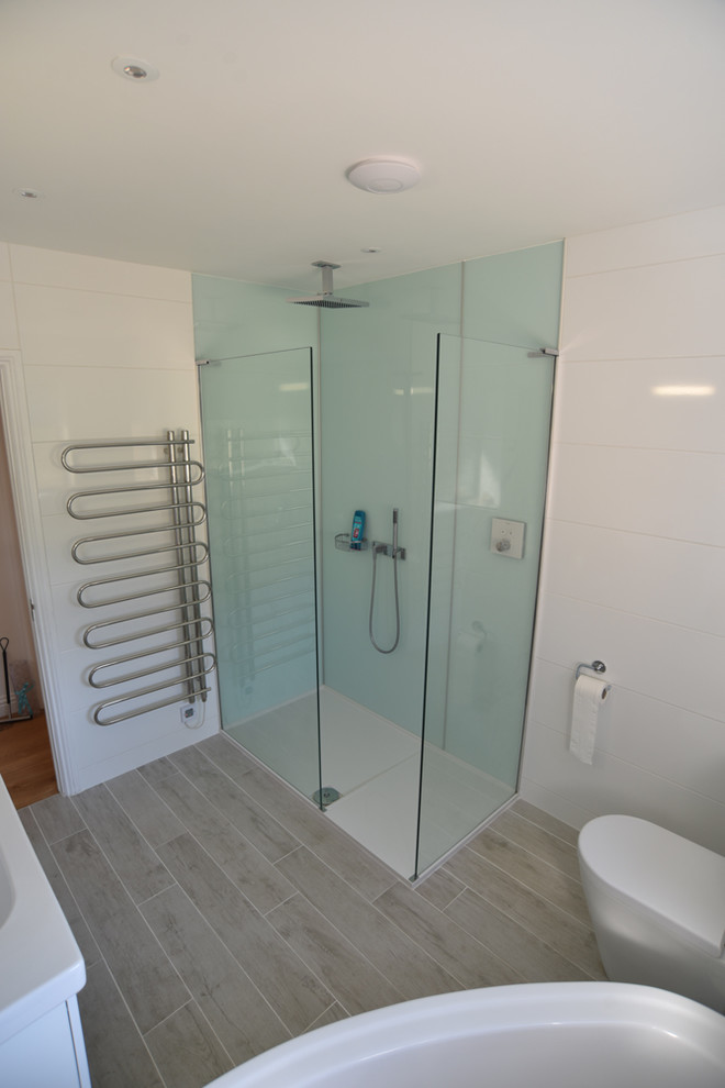 Design ideas for a medium sized modern ensuite bathroom in Dorset with flat-panel cabinets, white cabinets, a walk-in shower, a two-piece toilet, white tiles, ceramic tiles, white walls, porcelain flooring and a wall-mounted sink.