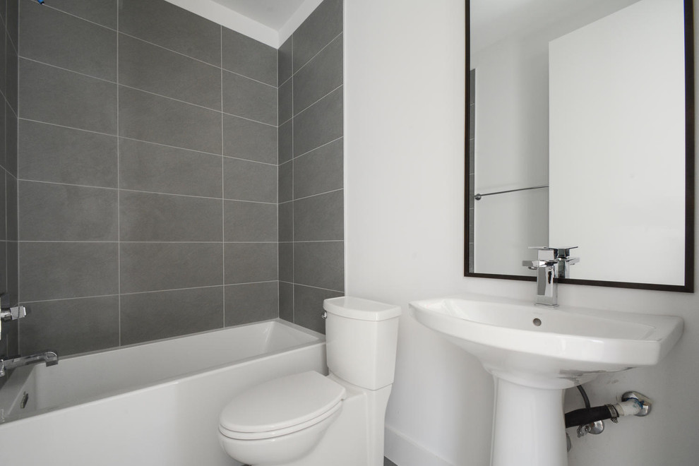 Modelo de cuarto de baño moderno de tamaño medio con paredes blancas, combinación de ducha y bañera, sanitario de dos piezas, aseo y ducha y lavabo con pedestal