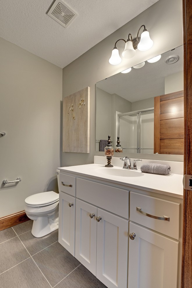 Mittelgroßes Klassisches Duschbad mit integriertem Waschbecken, Schrankfronten mit vertiefter Füllung, weißen Schränken, gefliestem Waschtisch, Duschnische, Toilette mit Aufsatzspülkasten, grauen Fliesen, Steinplatten, grauer Wandfarbe und Vinylboden in Minneapolis
