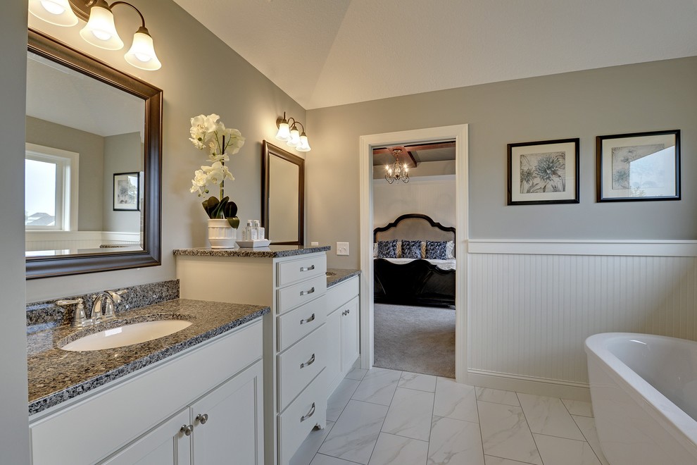 Foto på ett stort vintage en-suite badrum, med ett undermonterad handfat, luckor med infälld panel, vita skåp, granitbänkskiva, ett fristående badkar, en hörndusch, en toalettstol med hel cisternkåpa, vit kakel, stenkakel och grå väggar