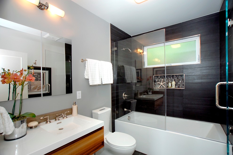 На фото: ванная комната среднего размера в современном стиле с плоскими фасадами, фасадами цвета дерева среднего тона, ванной в нише, душем над ванной, унитазом-моноблоком, черной плиткой, серыми стенами, душевой кабиной, монолитной раковиной, столешницей из кварцита, открытым душем и белой столешницей с