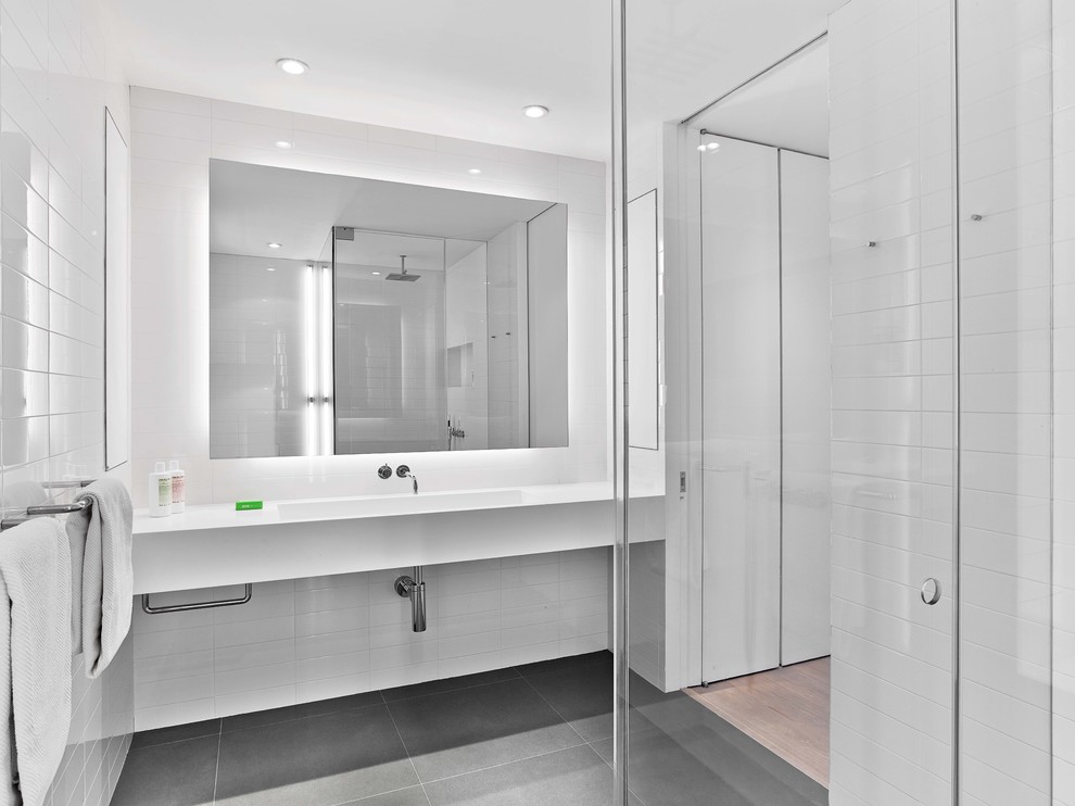 ニューヨークにあるモダンスタイルのおしゃれな浴室 (コーナー設置型シャワー、白いタイル、一体型シンク、グレーの床、白い洗面カウンター) の写真