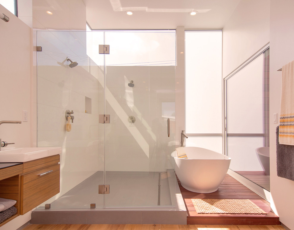 Inspiration pour une salle de bain principale design en bois brun avec une vasque, un placard à porte plane, un plan de toilette en verre, une baignoire indépendante, une douche ouverte, un carrelage blanc, des carreaux de céramique, un mur blanc et un sol en carrelage de porcelaine.