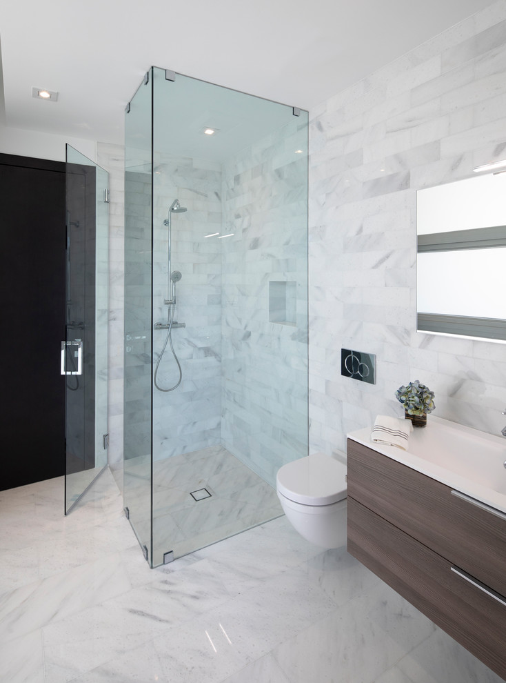 This is an example of a nautical bathroom in Miami with dark wood cabinets, a corner shower, a wall mounted toilet, white tiles, marble tiles, white walls, marble flooring, a hinged door and white worktops.