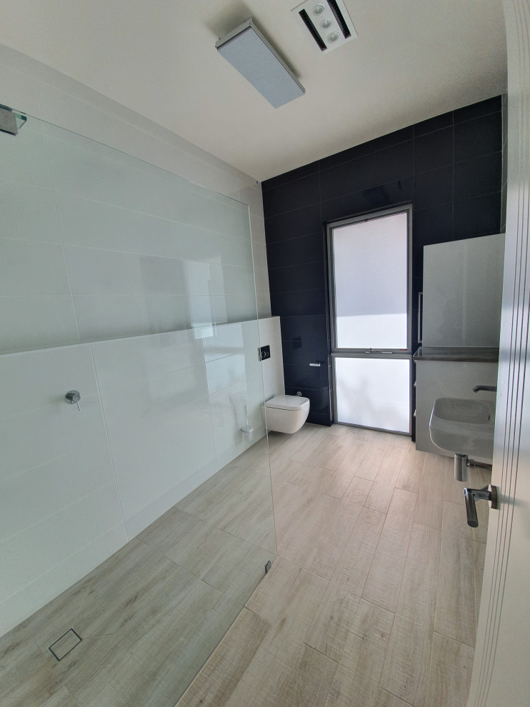 Foto på ett mellanstort funkis svart badrum, med en öppen dusch, en vägghängd toalettstol, svart kakel, keramikplattor, vita väggar, klinkergolv i keramik, bänkskiva i akrylsten, beiget golv och med dusch som är öppen