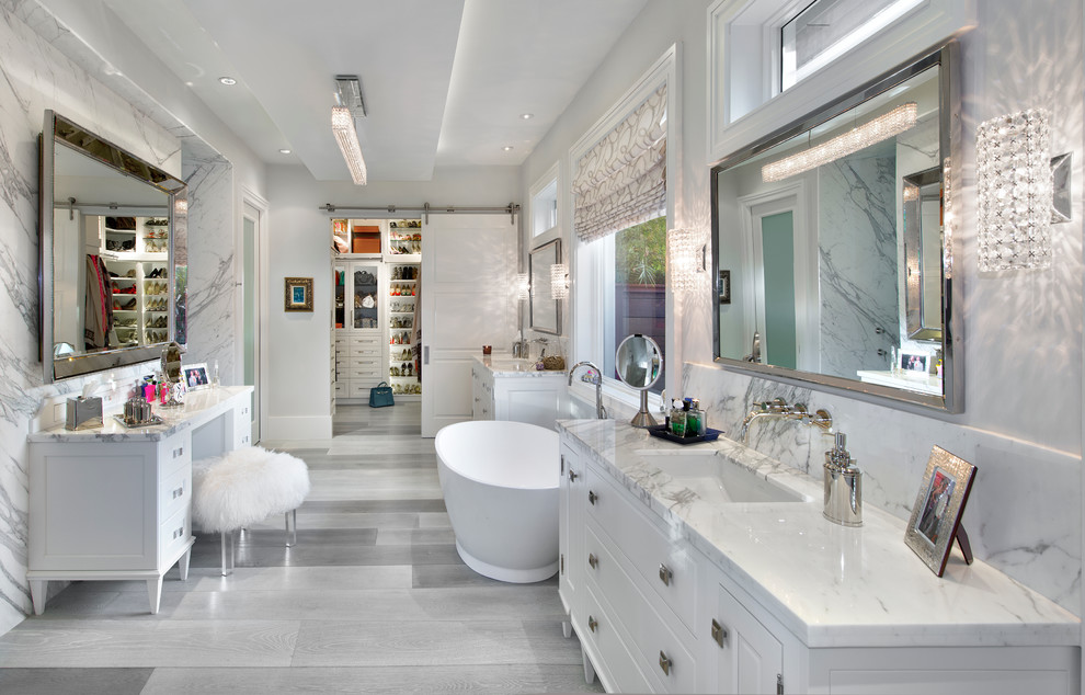 Cette image montre une salle de bain principale design avec un placard avec porte à panneau surélevé, des portes de placard blanches, un plan de toilette en marbre, une baignoire indépendante, un carrelage blanc, un mur blanc et un lavabo encastré.