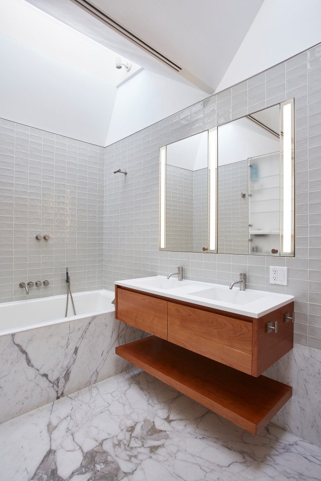 Foto på ett mellanstort funkis vit badrum med dusch, med släta luckor, skåp i mellenmörkt trä, ett badkar i en alkov, en dusch/badkar-kombination, grå kakel, porslinskakel, ett integrerad handfat och grått golv