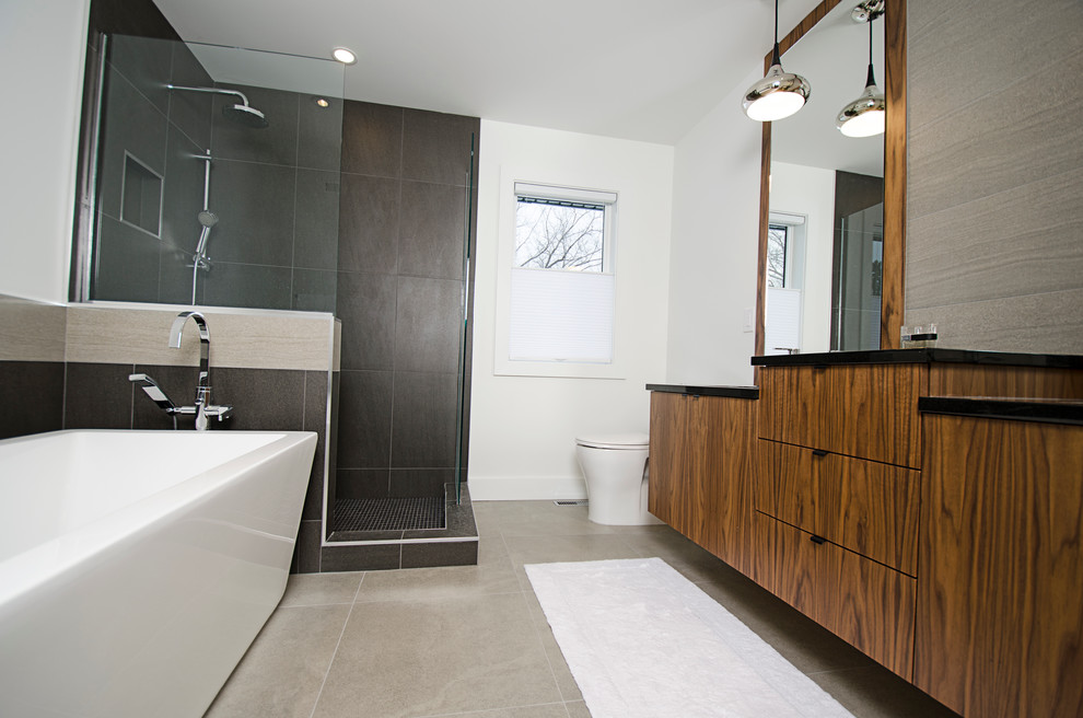 Medium sized contemporary ensuite bathroom in Other with a submerged sink, flat-panel cabinets, dark wood cabinets, granite worktops, a freestanding bath, a walk-in shower, a two-piece toilet, grey tiles, porcelain tiles, white walls, grey floors, an open shower and black worktops.
