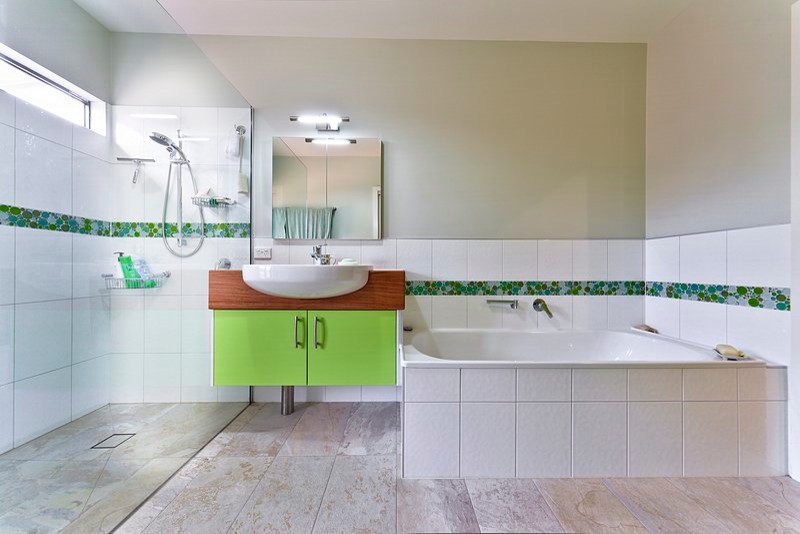 На фото: ванная комната среднего размера в стиле кантри с плоскими фасадами, зелеными фасадами, угловой ванной, угловым душем, зеленой плиткой, белой плиткой, полом из травертина, монолитной раковиной, столешницей из дерева и открытым душем с
